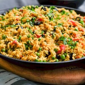 Colorful vegetable fried rice served in cast iron pan with fresh herbs, ideal for food photography.