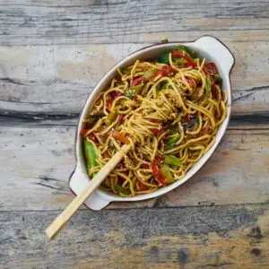 Colorful vegetable noodles with chopsticks on a rustic wooden table, showcasing a delicious, healthy meal.