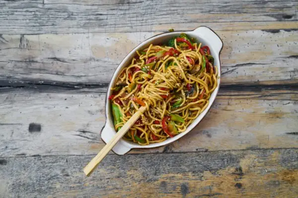 Colorful vegetable noodles with chopsticks on a rustic wooden table, showcasing a delicious, healthy meal.