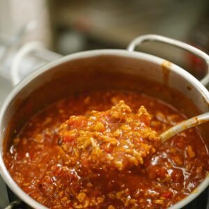 High angle freshly cooked yummy bolognese sauce in spoon and saucepan placed on stove in kitchen