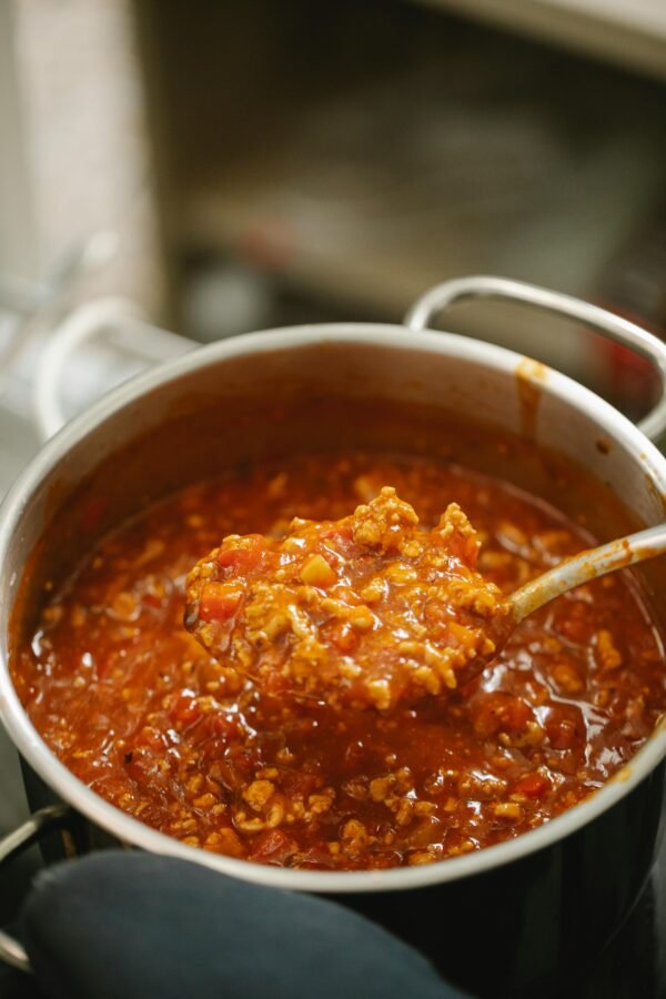 High angle freshly cooked yummy bolognese sauce in spoon and saucepan placed on stove in kitchen